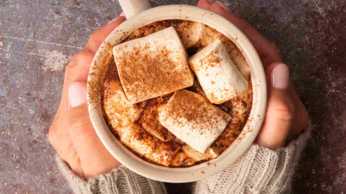 hands holding a cup of homemade coffee with marshmallows and cinnamon