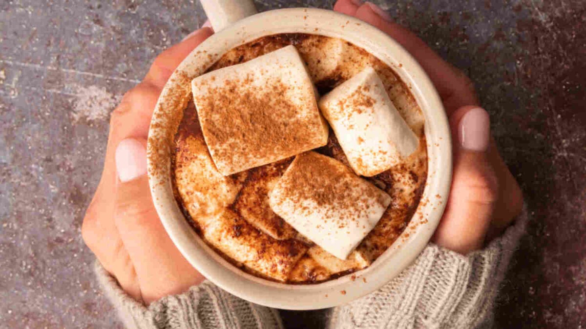hands holding a cup of homemade coffee with marshmallows and cinnamon