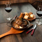 hearty family dinners depicted by this lamb shank with two glasses of red wine