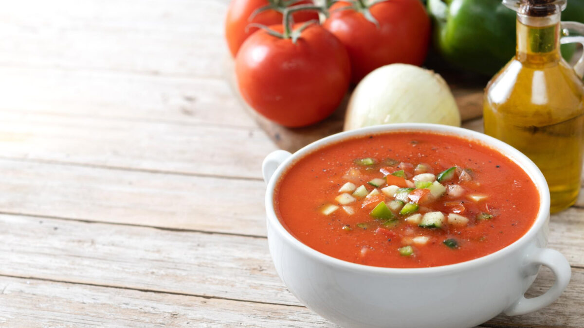 Cold soups made simple with a bowl of classic gazpacho and raw ingredients on a table