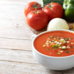 Cold soups made simple with a bowl of classic gazpacho and raw ingredients on a table