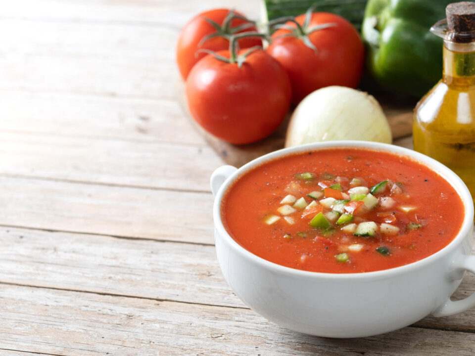 Cold soups made simple with a bowl of classic gazpacho and raw ingredients on a table