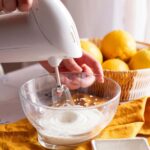 person using an electric whisk with a bowl of citrus fruit next to them, illustrating one of 5 smart baking hacks