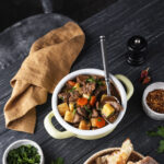 A rustic table set with classic homemade dishes including beef stew, bread pudding, and mashed potatoes, showcasing traditional old-school cooking.