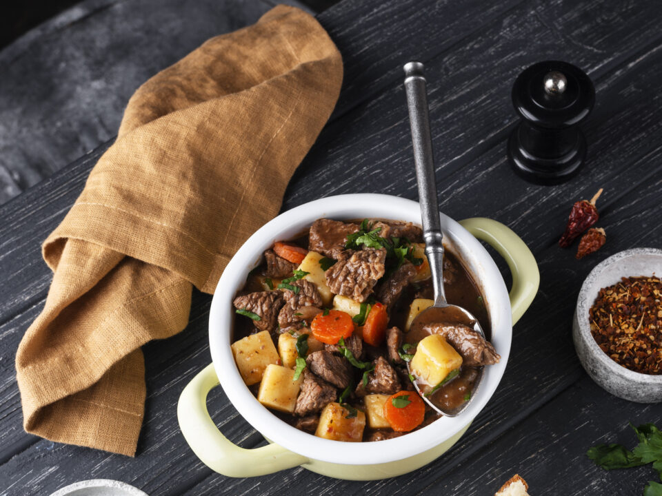 A rustic table set with classic homemade dishes including beef stew, bread pudding, and mashed potatoes, showcasing traditional old-school cooking.